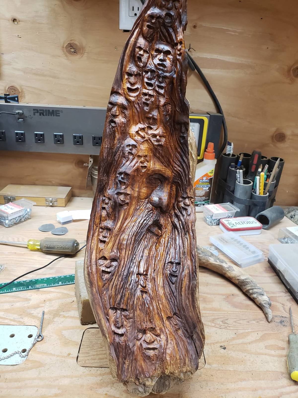 Wood spirit carving with a bearded face and dozens of smaller faces